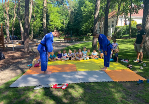 Dzieci siedzą na ziemi, patrzą na pokaz instruktorów judo